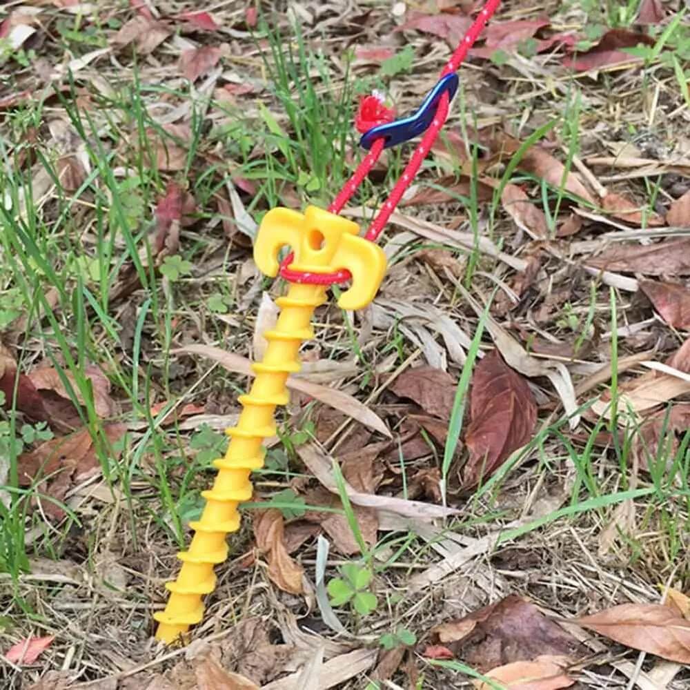 {{Camping Gear {{ Hiking Gear }} }} - {{Tac Treasure Shop }} {{  Yellow Screw design tent stake. Red tiecord attached, ready to putinto the ground. Grass and leaves cover the surface.}}